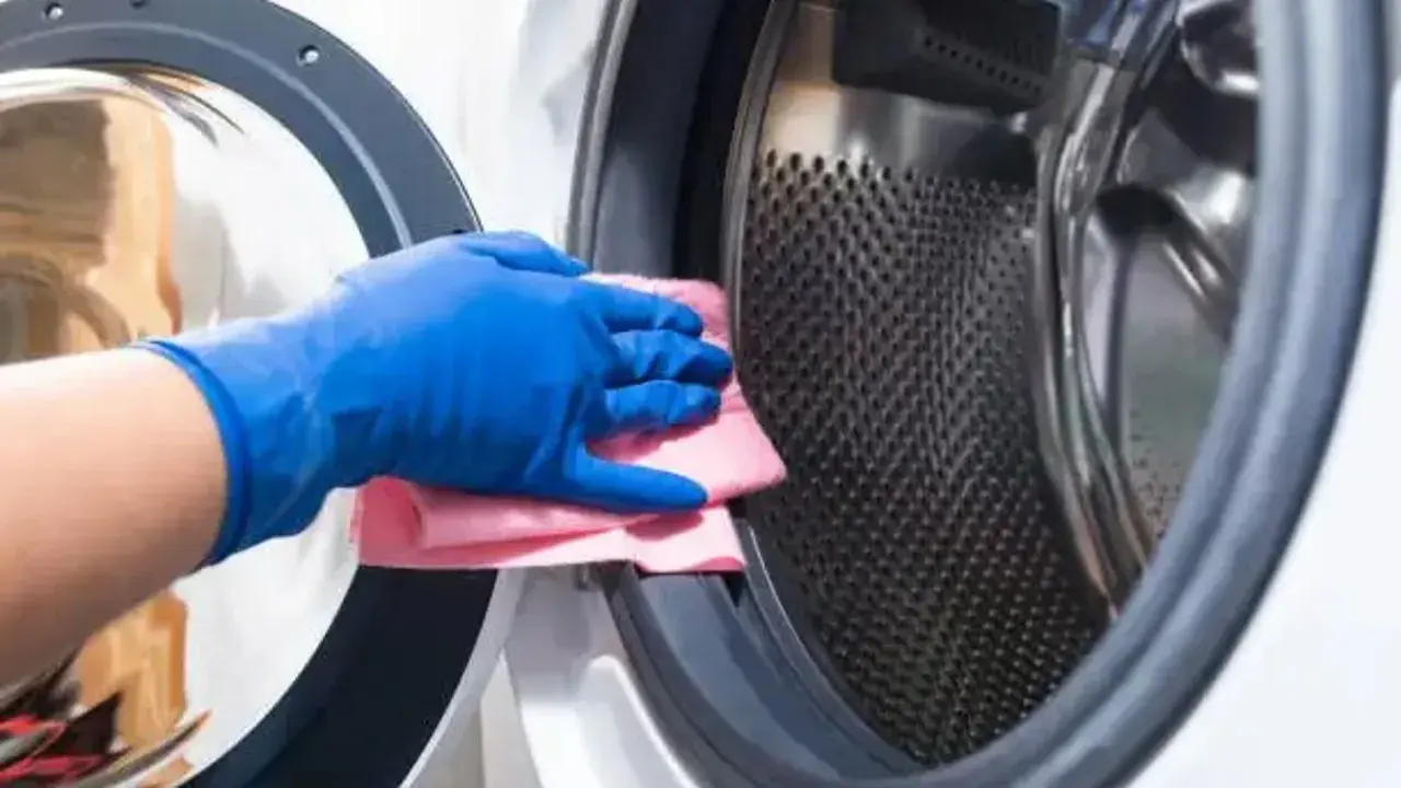 Mano con guante azul limpiando la goma de la lavadora con un paño rosa.