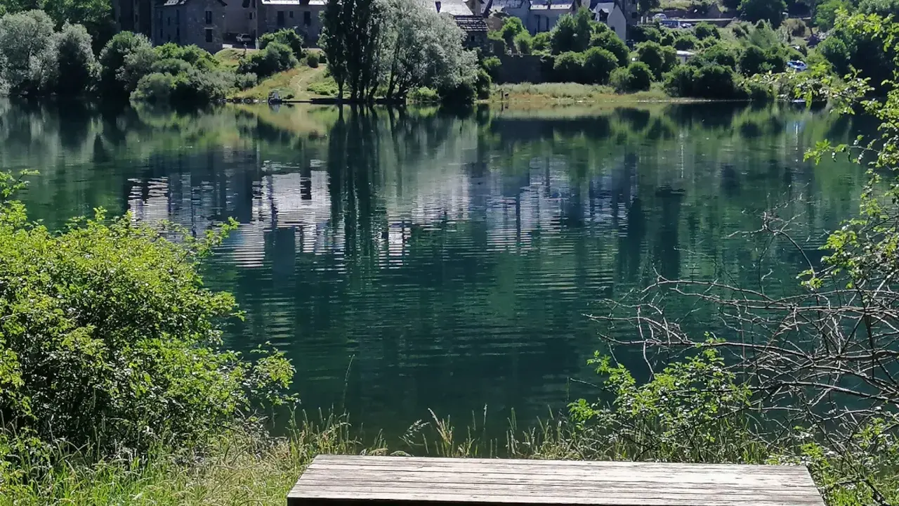 Un banco de madera invita a contemplar el embalse de Lanuza, con un pueblo de tejados grises reflejado en sus tranquilas aguas verdes.