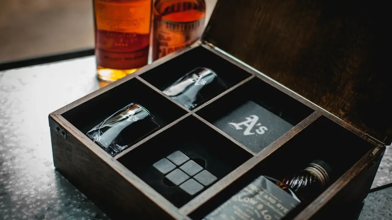 Elegancki zestaw z whisky w drewnianej skrzynce: dwie butelki, kieliszki z monogramem "A's", kamienie do whisky i podkładka.