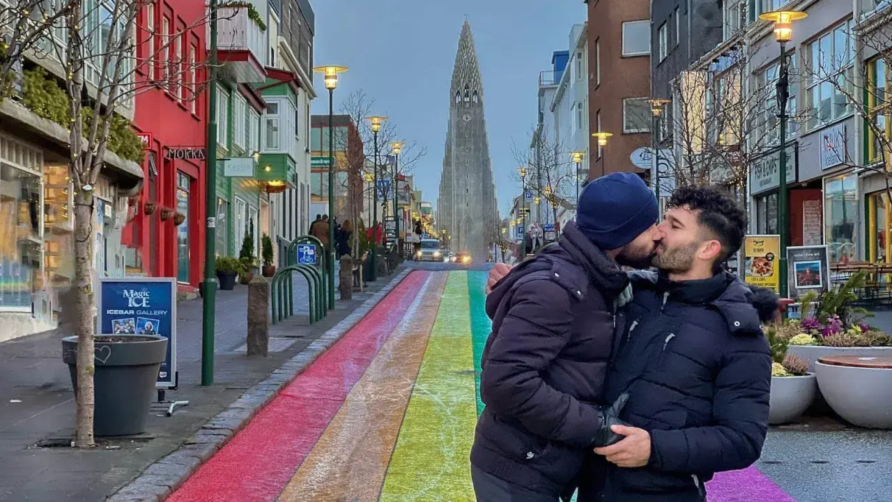 A couple shares a kiss on a rainbow-painted street in gay Reykjavik, with Hallgrímskirkja church in the background.