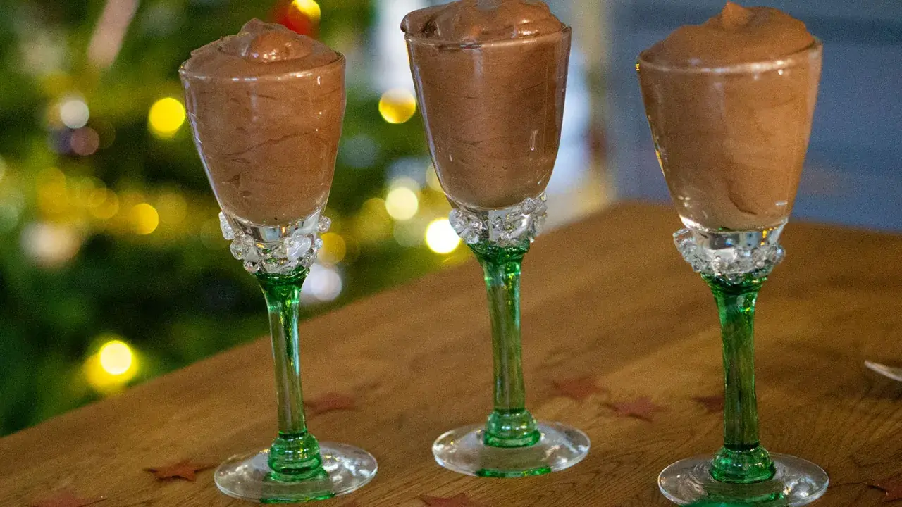 Tre glas med krämig chokladmousse, perfekta för ett enkelt chokladmousse recept. Julbelysning i bakgrunden skapar en festlig stämning.