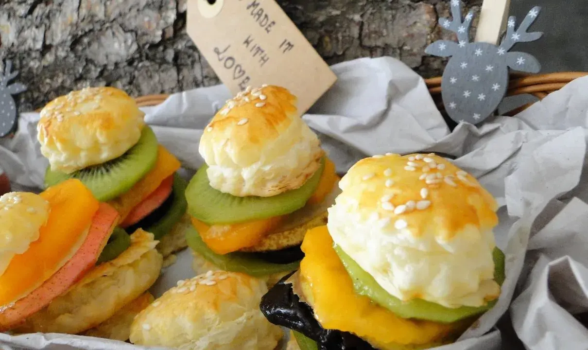 Mini burgery z ciasta francuskiego z owocami: kiwi, mango, brzoskwinia i różowa wędlina. Wyglądają jak małe dzieła sztuki.