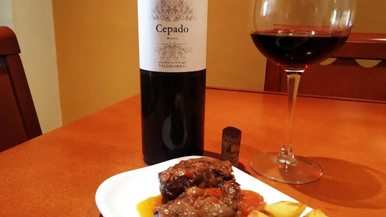 Un plato de carrilleras estofadas con patatas, acompañado de una copa de vino tinto Cepado Mencía, ideal para maridar.