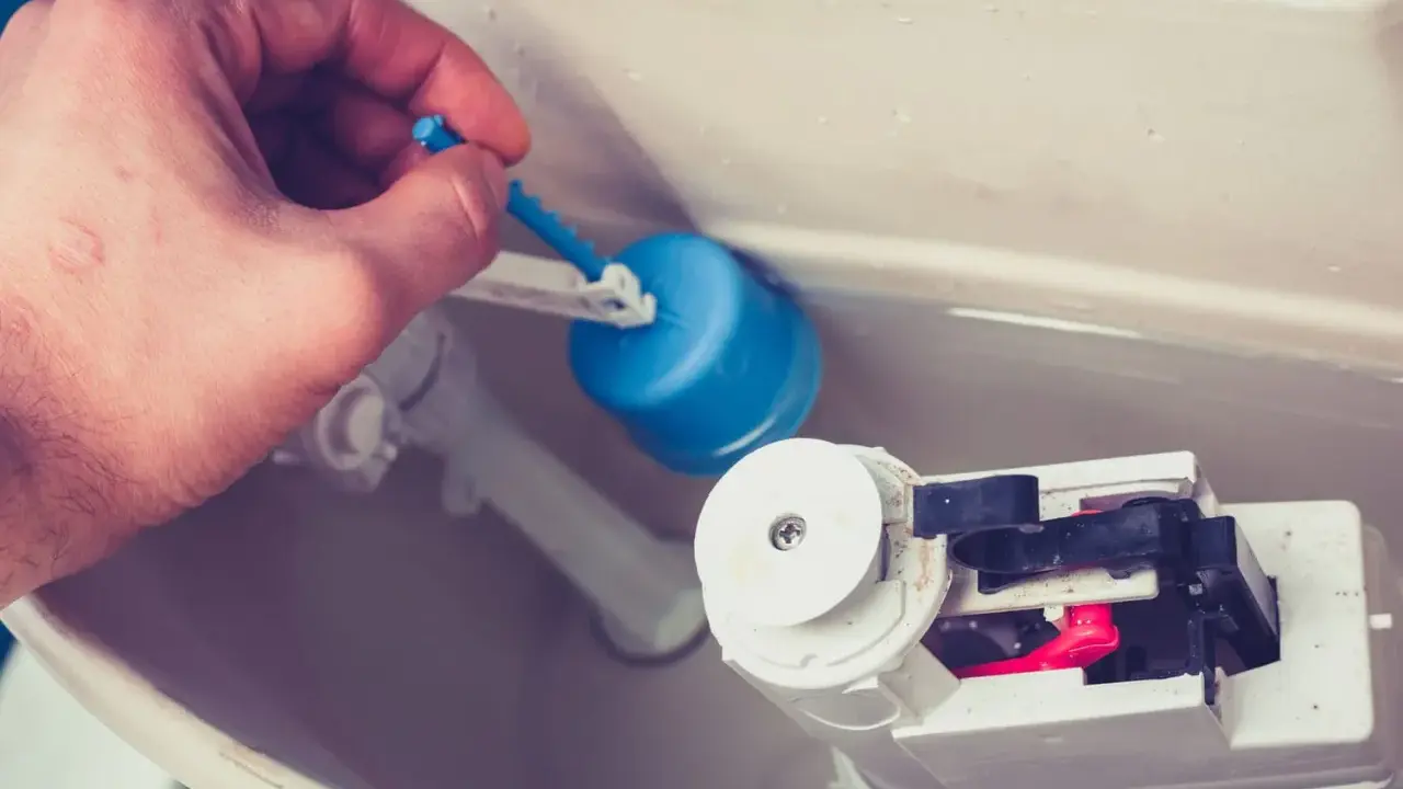 Main tenant répare chasse d'eau bouton poussoir. Il ajuste le flotteur bleu pour un bon fonctionnement.