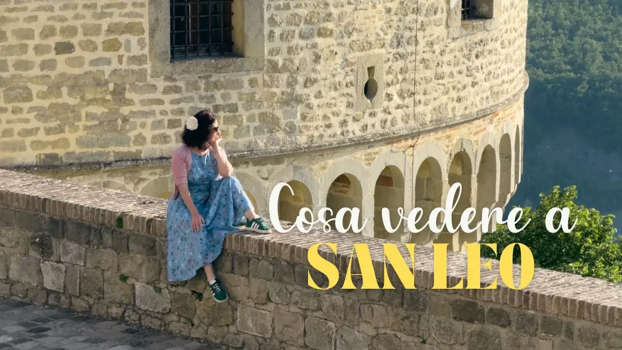 Donna seduta su un muretto di pietra, con vista panoramica. Un'ottima pausa durante il trekking a San Leo.