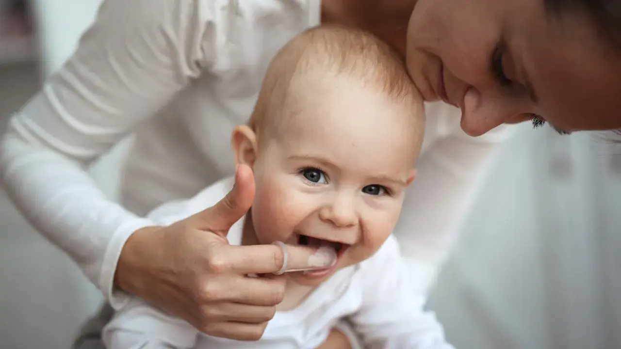 Mama pomaga dziecku z kolejnością wychodzenia zębów, delikatnie masując dziąsła palcem w nakładce.