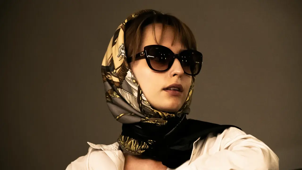 Donna con occhiali da sole e un elegante outfit con foulard annodato al collo, che incornicia il viso.