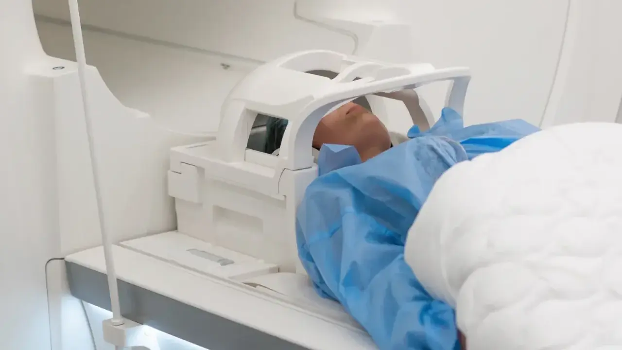 Pacjent w niebieskim fartuchu leży w aparacie MRI. Czas badania, czyli ile trwa rezonans głowy, zależy od wielu czynników.