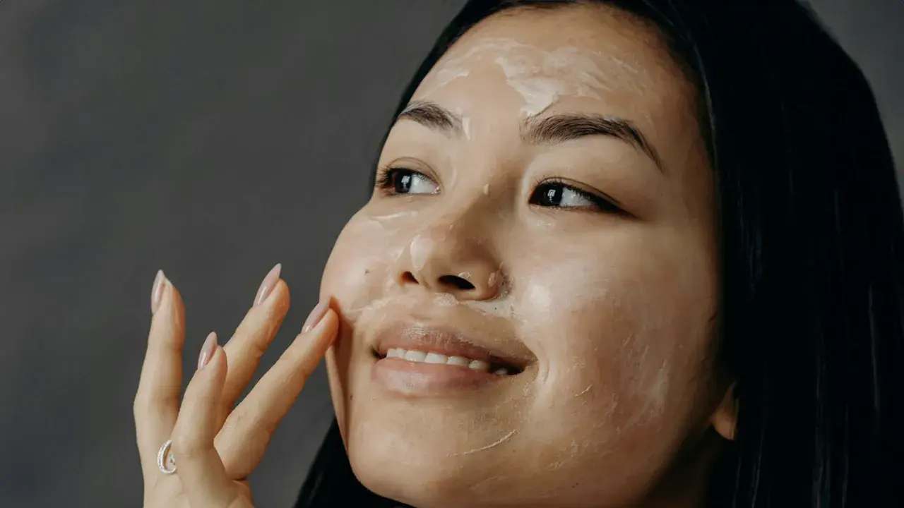 Donna applica una crema sul viso, un gesto quotidiano per come curare la pelle del viso.