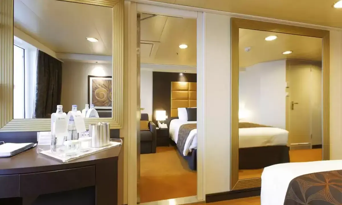 Interno di una cabina MSC Divina con balcone. Letto, specchi e un tavolino con bottiglie d'acqua.