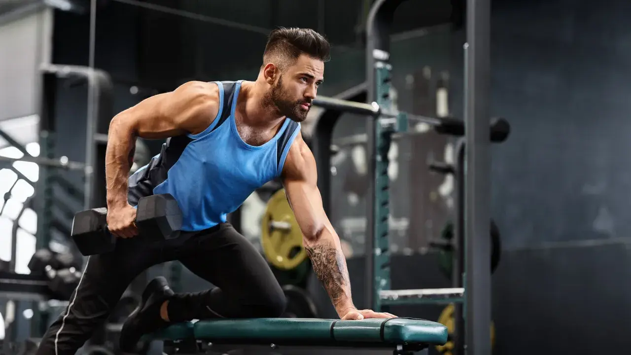 Mann mit Bart macht einbeiniges Rudern mit Kurzhantel. Fokus auf Muskelaufbau Training im Fitnessstudio.