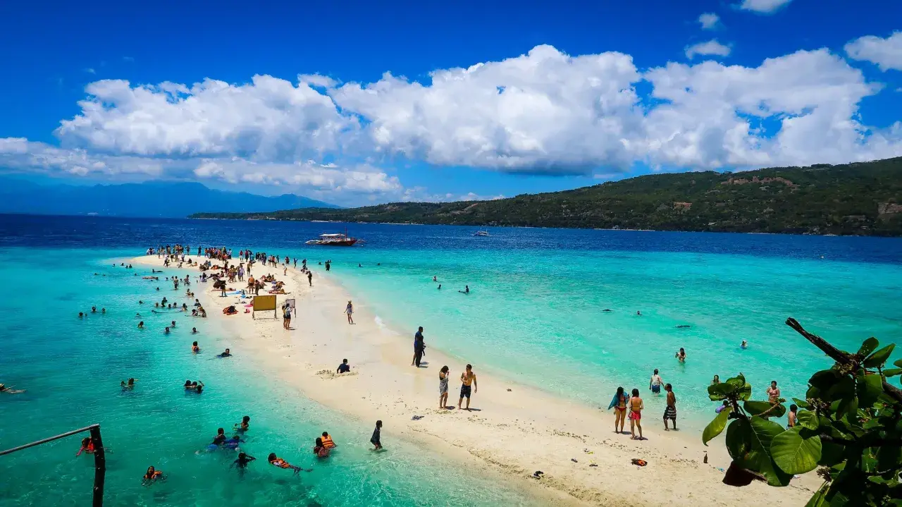 Plaża na Filipinach z turystami kąpiącymi się w turkusowej wodzie i spacerującymi po piaszczystym brzegu.