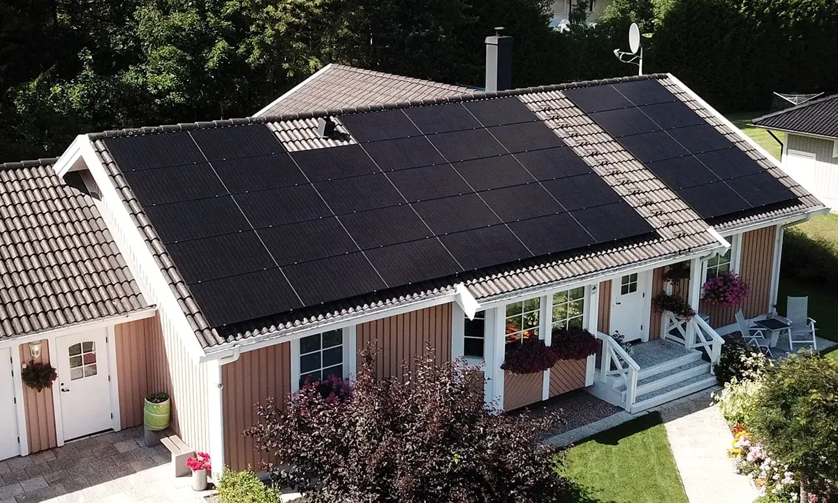 Ett hus med mörka solceller på taket, som fångar solens energi för ett grönare hem.