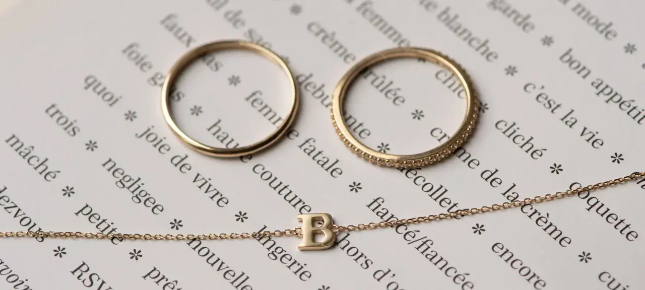 Anelli e collana in oro 14 carati, che significa un gioiello di qualità, su pagine di un libro con parole francesi.