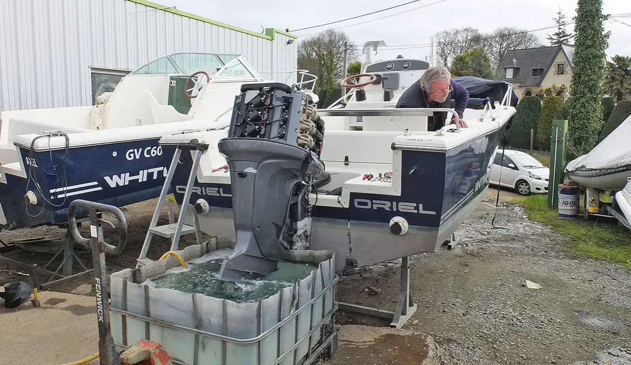 Un homme effectue le rinçage moteur hors bord vinaigre blanc d'un bateau. L'hélice est immergée dans une cuve remplie de liquide.