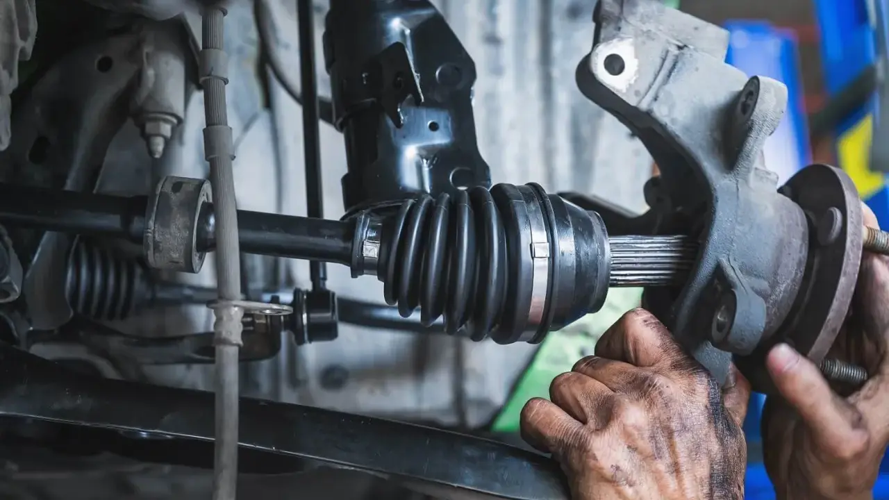 Mechanik wymienia uszkodzoną półoś, która powoduje wibracje. Widać gumową osłonę przegubu i zębaty wałek.