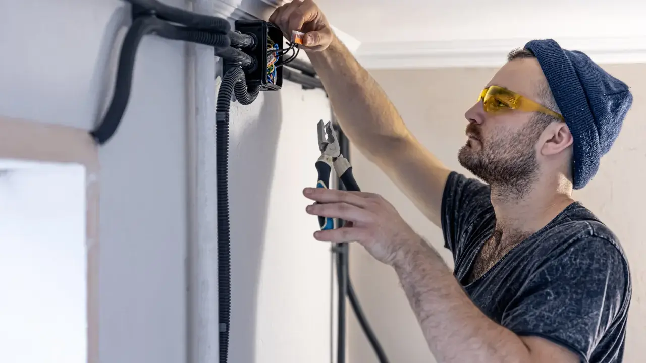 Elektryk w okularach ochronnych montuje przewody bezhalogenowe w puszce instalacyjnej, używając szczypiec.