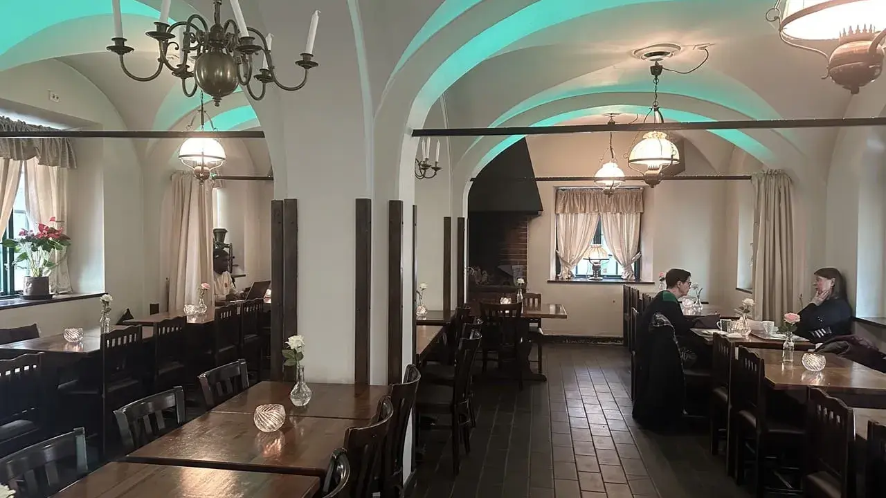 Mysig interiör på Cafe Kronhuset med välvda tak och varma ljus. Två personer sitter vid ett bord och samtalar.