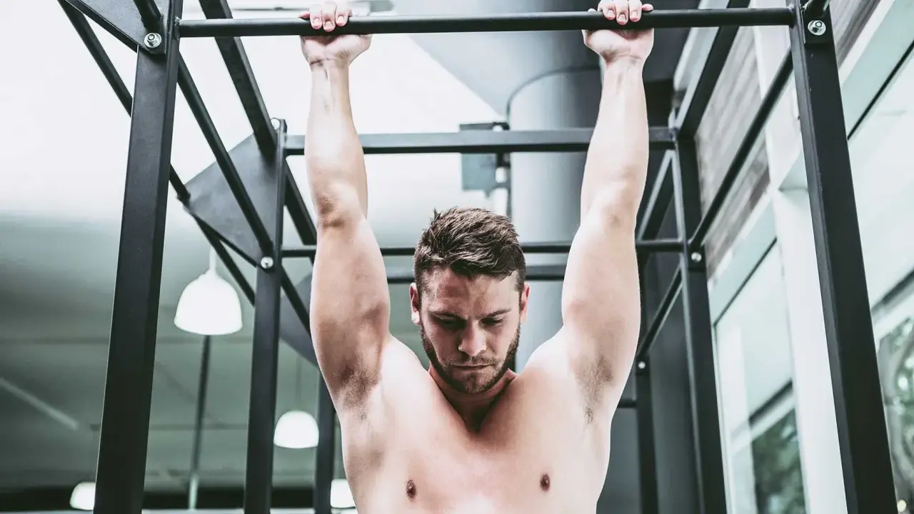 Uomo a torso nudo esegue trazioni alla sbarra, concentrato sul movimento per rafforzare la muscolatura.