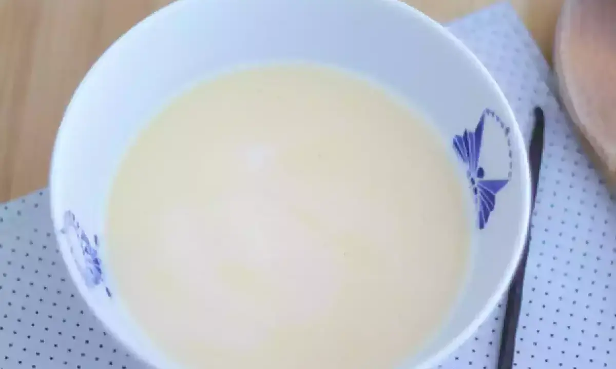 En skål med krämig vaniljsås, perfekt för ditt vaniljsås recept. En vaniljstång ligger bredvid.