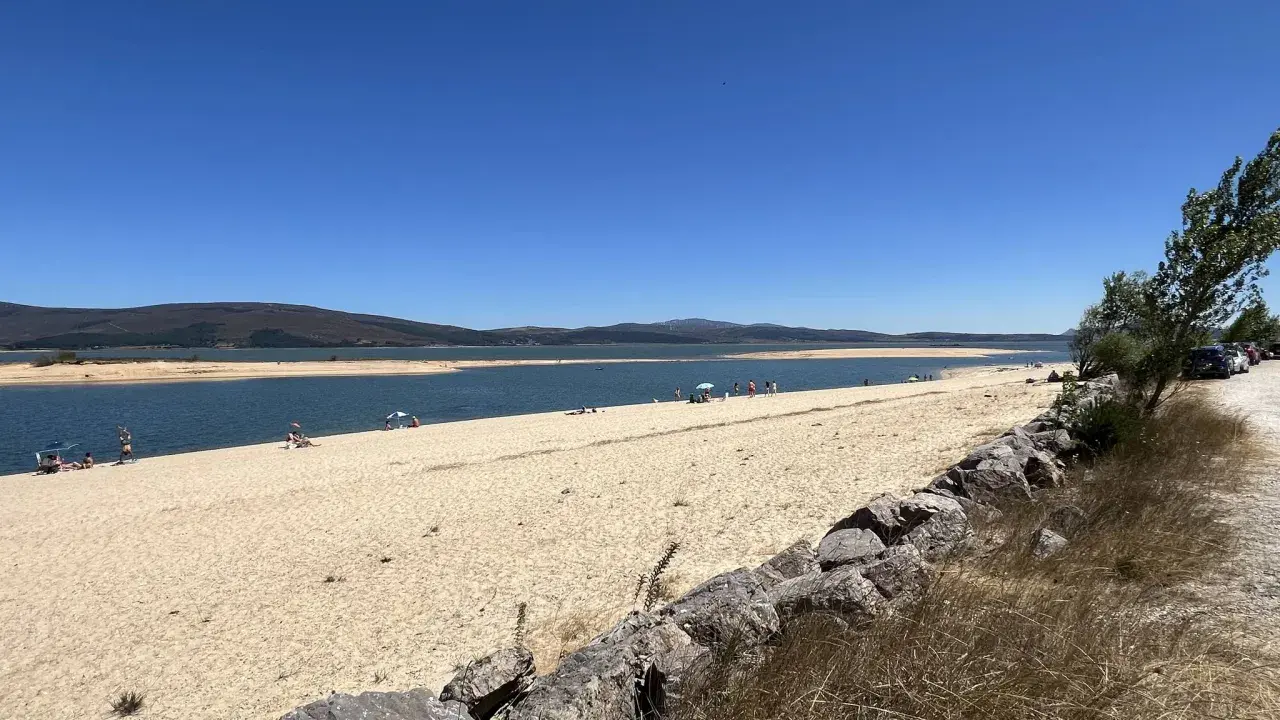 Gente disfrutando del sol y el agua en la playa de Arija, con montañas al fondo y un cielo azul despejado.