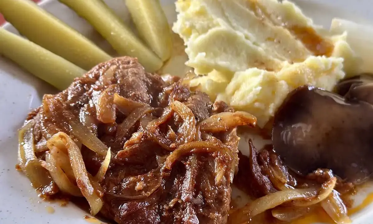 Karkówka pieczona w plastrach z cebulą, podana z puree ziemniaczanym, ogórkami kiszonymi i grzybami.