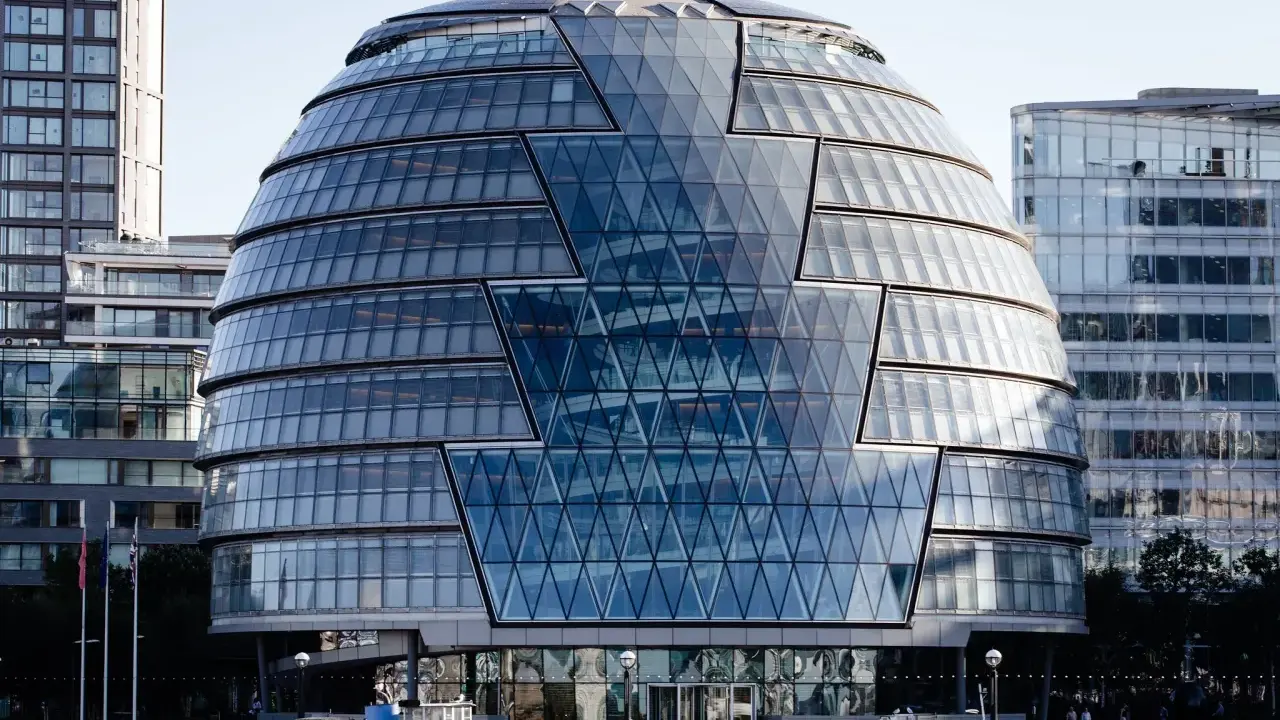 Edificio iconico di Norman Foster, con facciata a diamante in vetro, riflette il cielo e gli edifici circostanti.