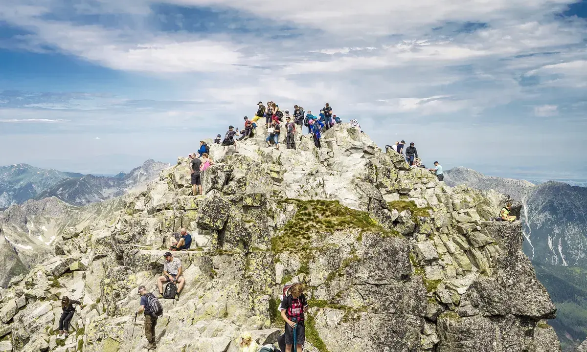 Tłum turystów na skalistym szczycie Rysów, podziwiający panoramę Tatr.