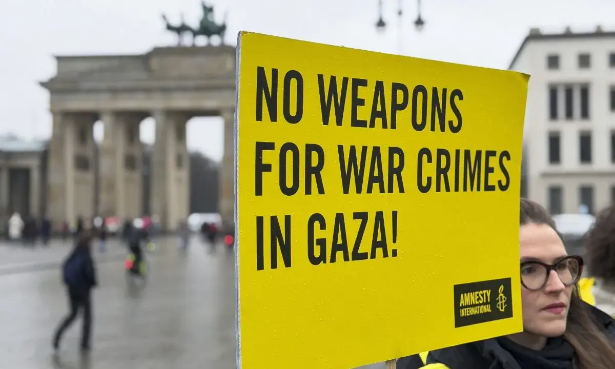 Gelbe Tafel mit Aufschrift "NO WEAPONS FOR WAR CRIMES IN GAZA!" vor dem Brandenburger Tor. Amnesty International setzt sich für Menschenrechte ein.