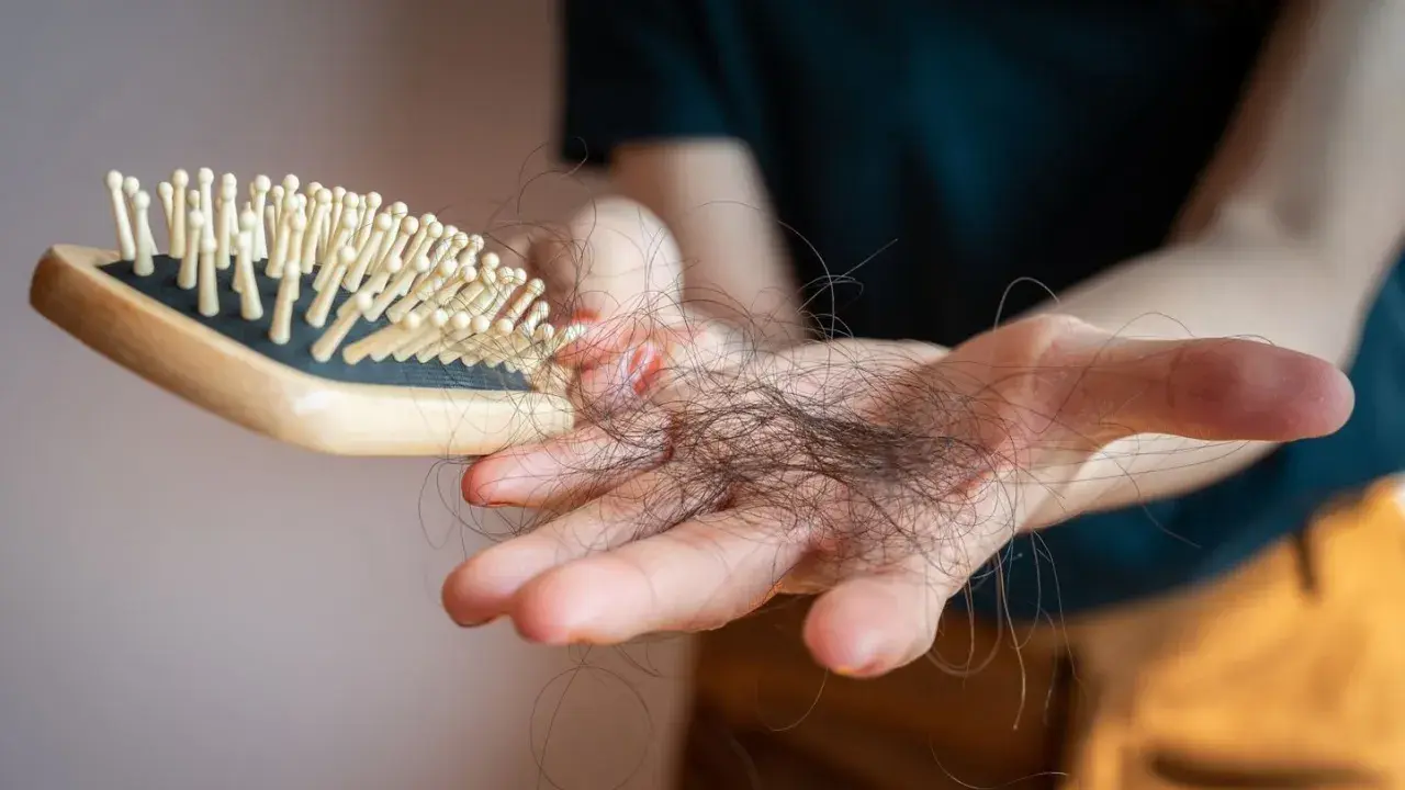 Main d'une personne tenant une brosse à cheveux avec des cheveux tombés, un effet secondaire possible du covid et perte de cheveux.