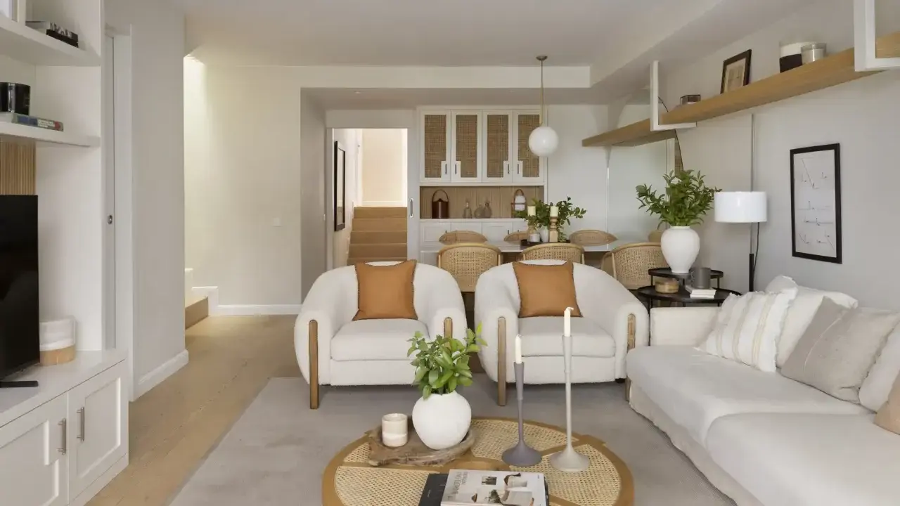 Salón rectangular dos ambientes con sofás blancos, sillones de borrego y mesa de centro de ratán.