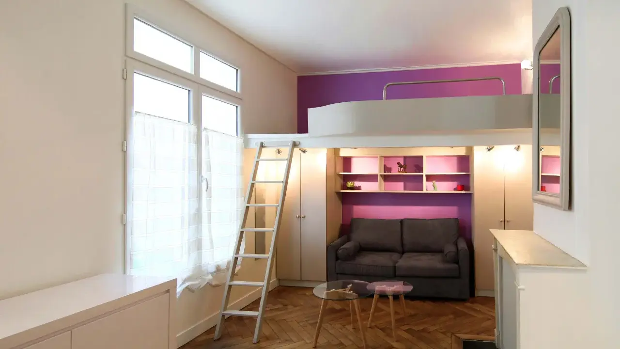 Aménagement petit studio optimisé avec lit mezzanine, canapé confortable et rangements intégrés. Un espace de vie fonctionnel et stylé.