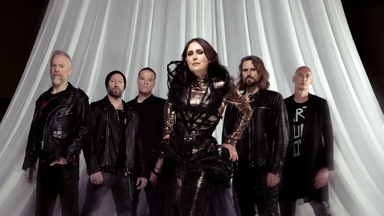 Within Temptation Sverige: Sharon den Adel i sin glittrande klänning, omgiven av bandmedlemmar i mörka kläder, framför en vit draperad bakgrund.