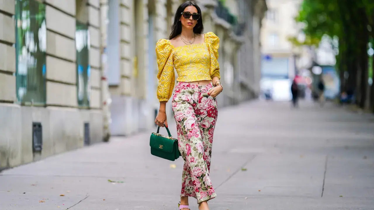 A woman shows that a woman can wear pants for cocktail attire, sporting a yellow puff-sleeve top and floral pants.