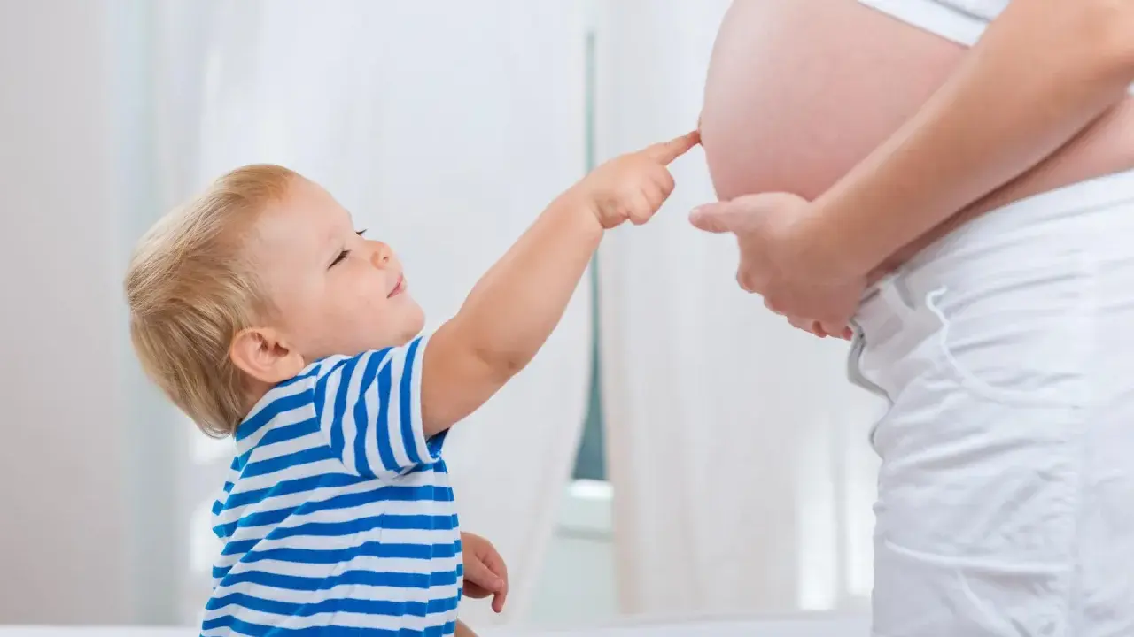 Mały chłopiec w pasiastej koszulce dotyka paluszkiem brzucha mamy, która jest w 25 tygodniu ciąży.