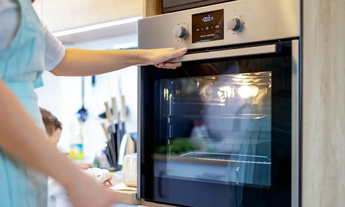 Une main ajuste la porte d'un four encastrable. La lumière intérieure est allumée, prêt pour la cuisson.