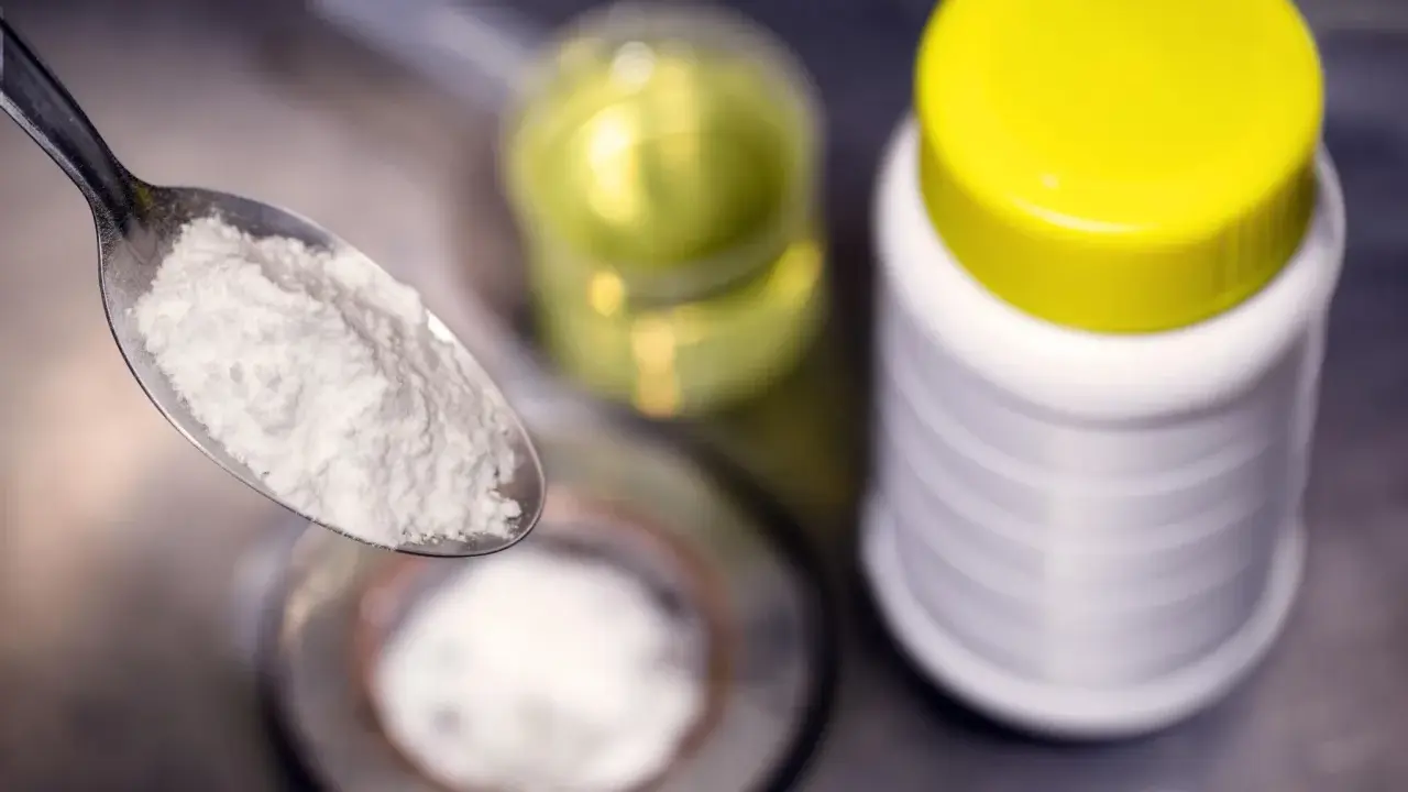 Ein Löffel mit weißem Pulver, bereit für die Reaktion mit Essig. Daneben ein Behälter mit Natron und eine Flasche mit Flüssigkeit.
