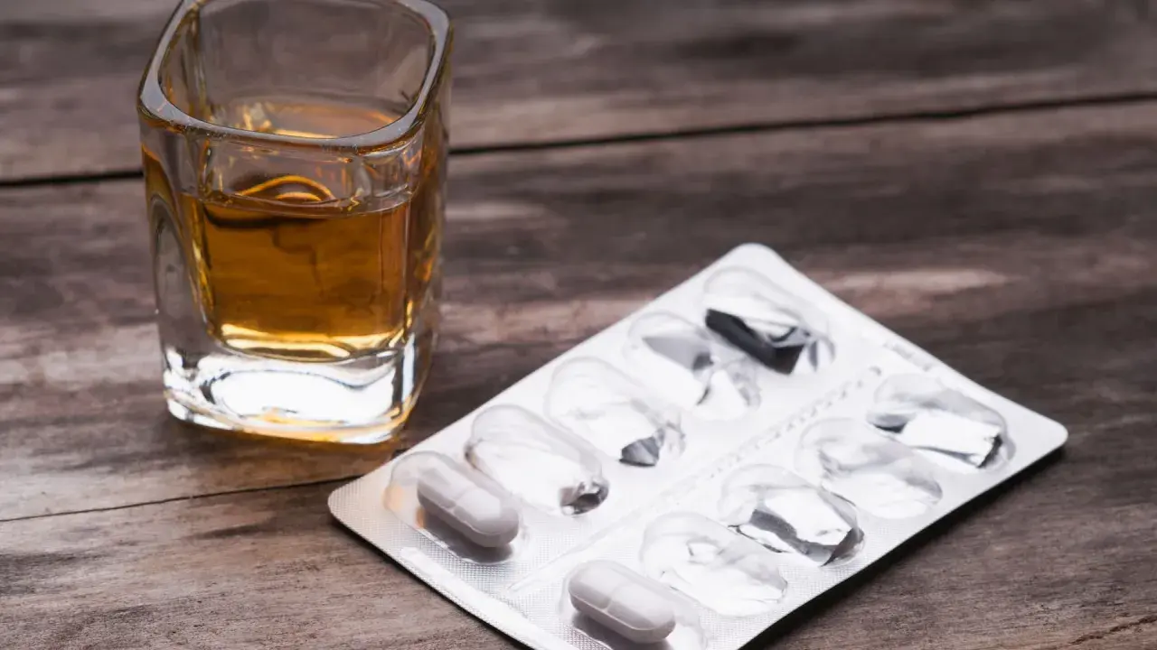 Ein Glas mit bernsteinfarbener Flüssigkeit und eine Blisterpackung mit einigen verbleibenden Pillen. Die Kombination von paracetamol und alkohol kann gefährlich sein.