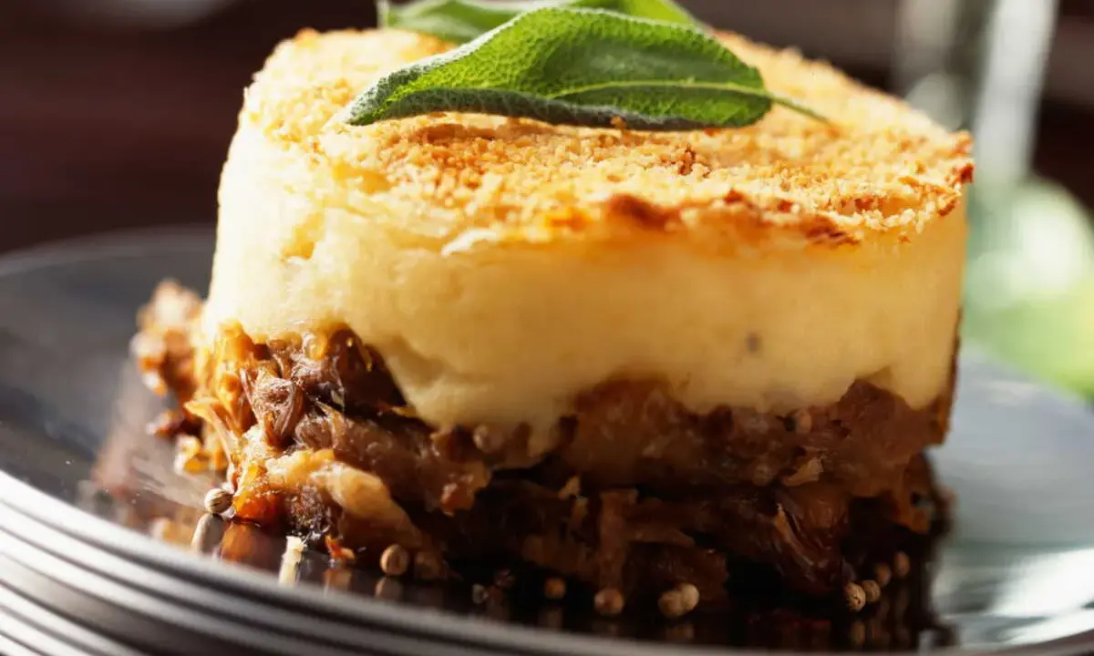 Un délicieux parmentier de canard, gratiné et garni d'une feuille de sauge, servi sur une assiette élégante.