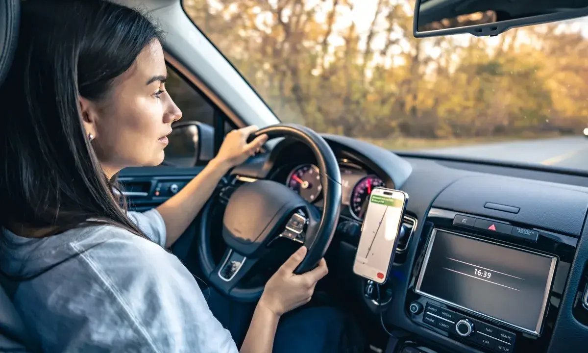 Kobieta prowadzi auto, a telefon z nawigacją zamontowany jest na desce rozdzielczej. Idealne miejsce, gdzie zamontować uchwyt na telefon w samochodzie.