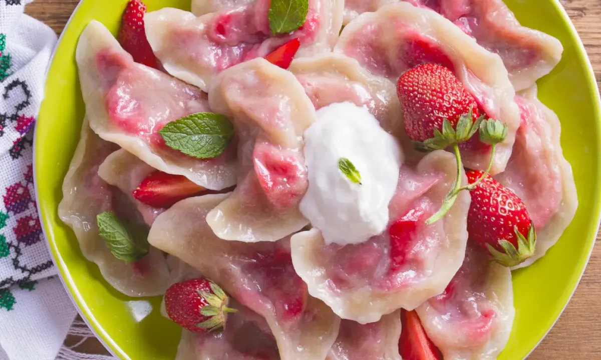 Pyszne pierogi z truskawkami, udekorowane miętą i śmietaną, na zielonym talerzu.