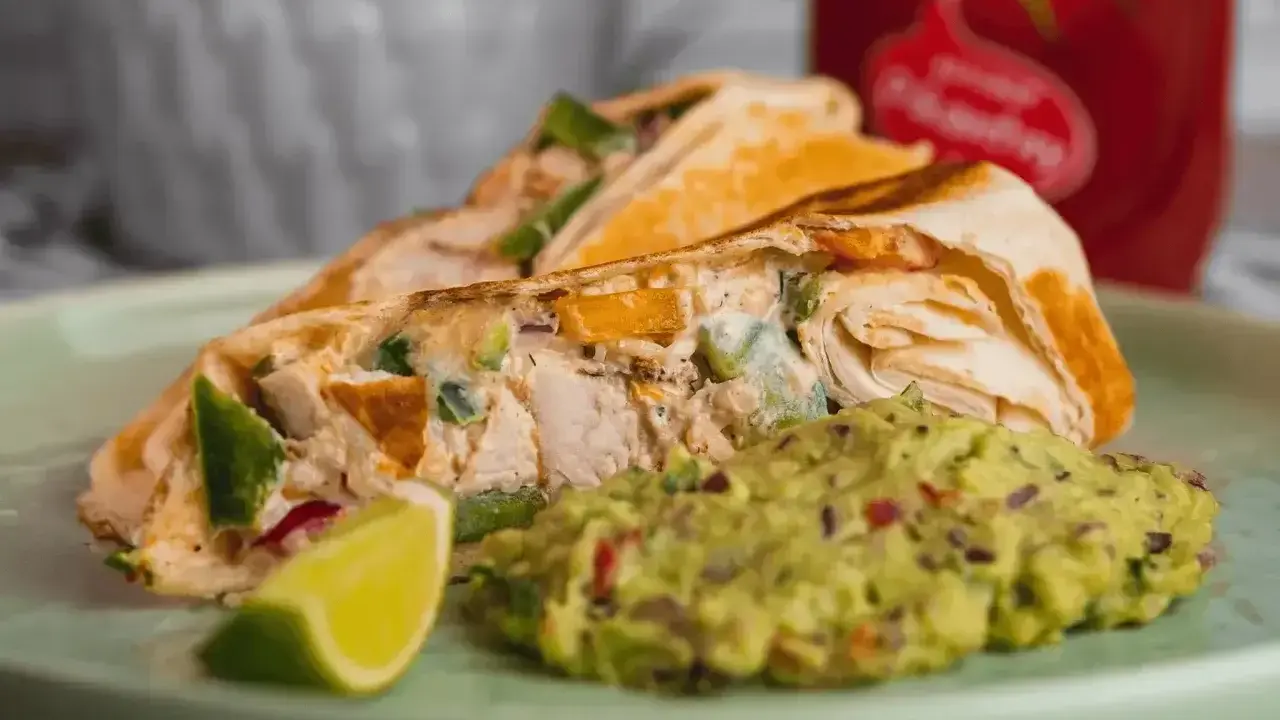 Roladka z tortilli z kurczakiem i warzywami, podana z guacamole i ćwiartką limonki. Idealny sos do tortilli!