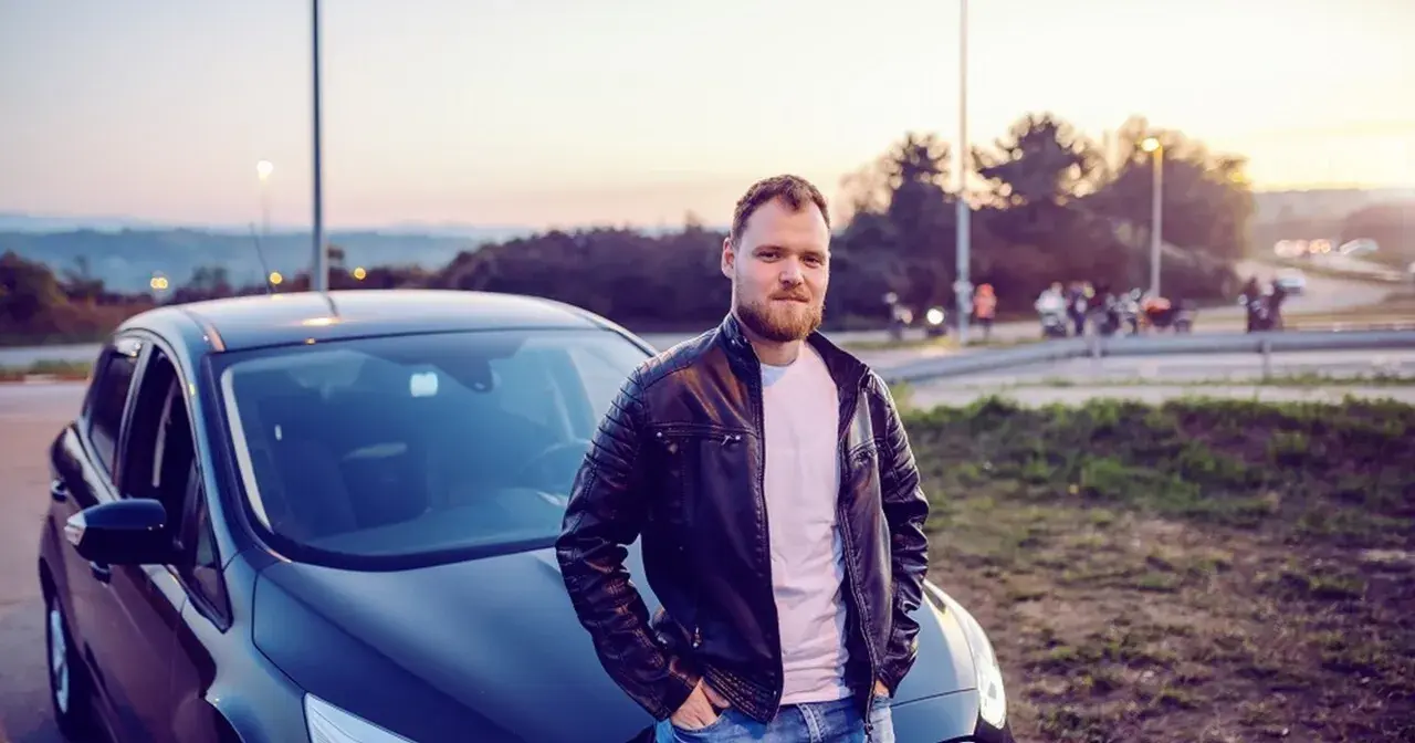 Mężczyzna w skórzanej kurtce opiera się o swój nowy samochód. To jego oc mubi, gotowy na przygodę.