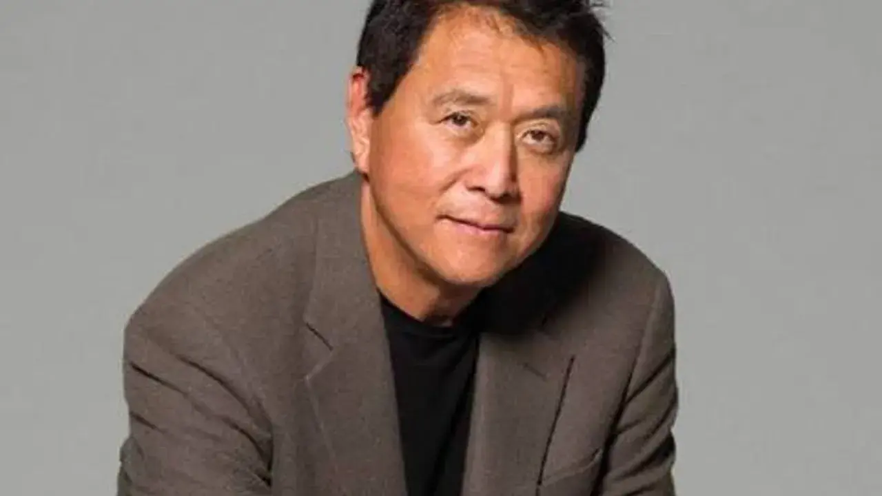 Robert Kiyosaki, autor "Bogatych ojców", w brązowej marynarce i czarnej koszulce, patrzy w obiektyw.
