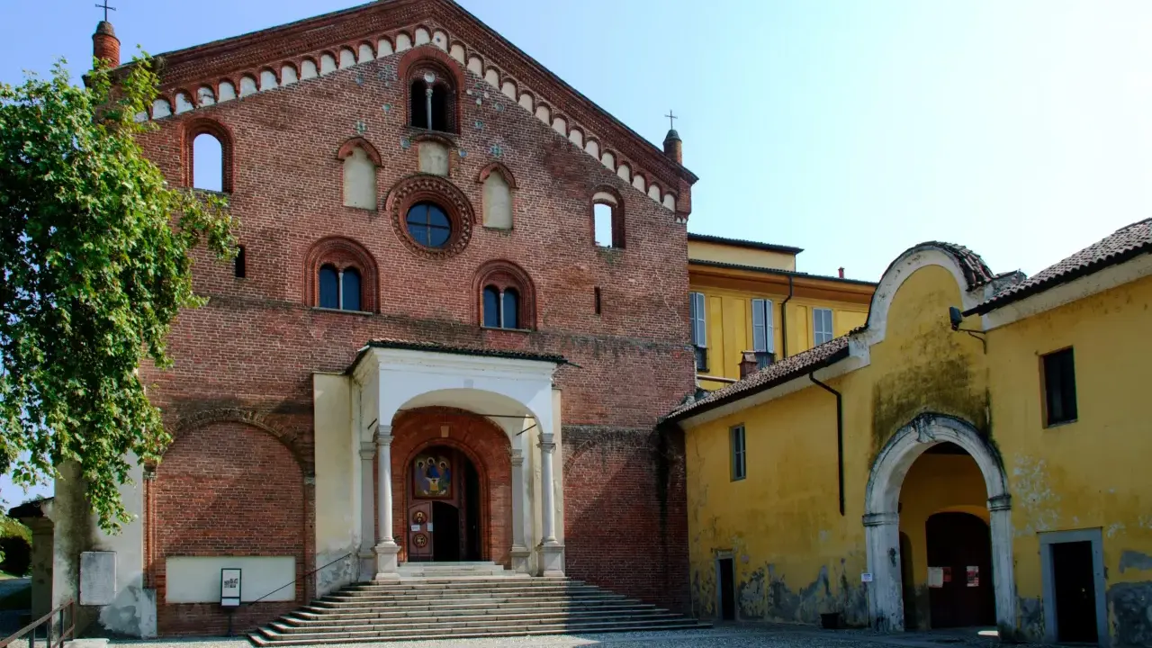 Morimondo cosa vedere: imponente facciata in mattoni rossi di un'antica abbazia, con scalinata e portico. Accanto, un edificio giallo con un arco.