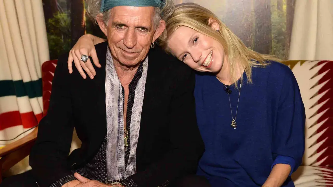 Keith Richards och en ung kvinna ler mot kameran. Hon vilar huvudet mot hans axel.