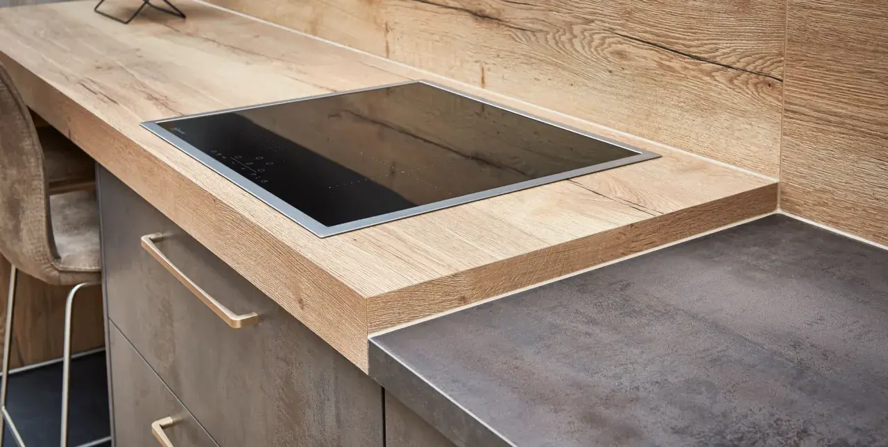 Eine moderne Küche mit einer Holzoptik-Arbeitsplatte und einem dunklen Stein-Arbeitsplatten-Material. Ein Kochfeld ist eingelassen.