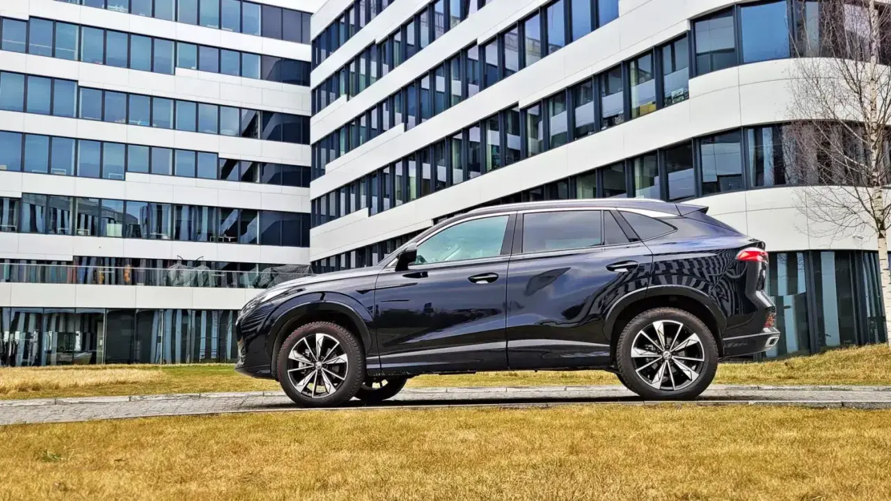 Czarny SUV MG HS, z nowoczesnym designem, zaparkowany przed biurowcem. Jego linia nadwozia sugeruje dynamiczne osiągi i niskie spalanie.
