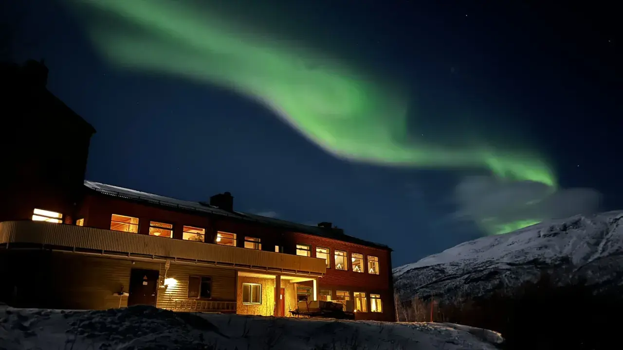 Norrsken över ett snötäckt landskap med ett hus. Perfekt för kiruna sightseeing turer.