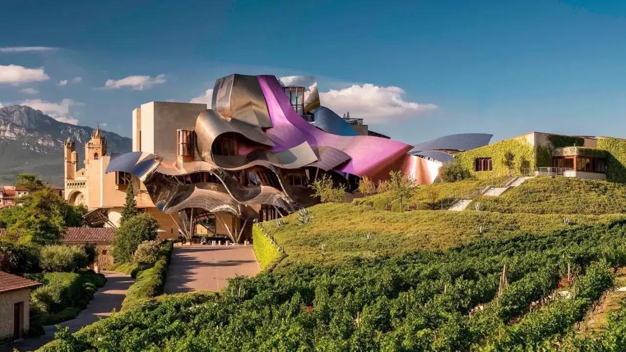 Edificio vanguardista con tejados curvos y viñedos en primer plano. Un ejemplo de alojamientos originales España, donde la arquitectura se fusiona con la naturaleza.